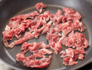 frying steak in a pan for cheesesteak recipe