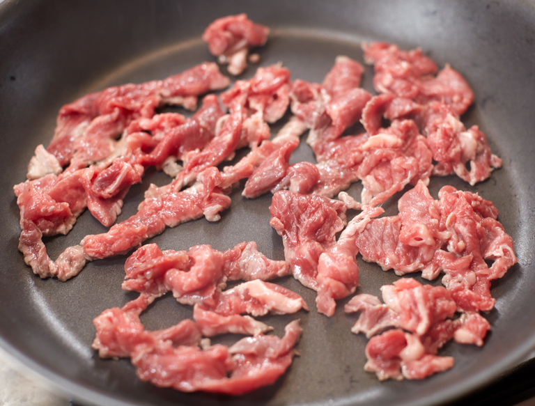 frying steak in a pan for cheesesteak recipe