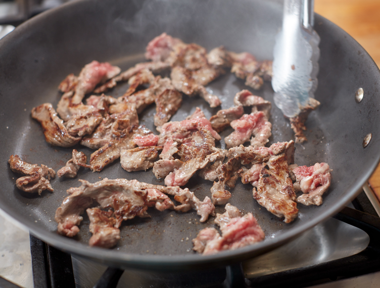 frying steak in a pan for cheesesteak recipe
